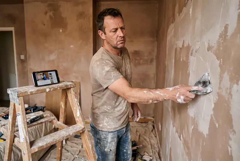 Homeowner attempting DIY skim coating on a bedroom wall with visible trowel marks